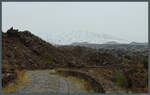 Östlich von Bronte dehnen sich die Lavafelder des Ätna aus, der im Hintergrund schneebedeckt aus dem Dunst hervortritt.